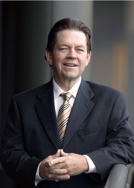 Headshot of Arthur Laffer smiling, hands folded, in black suit and tie